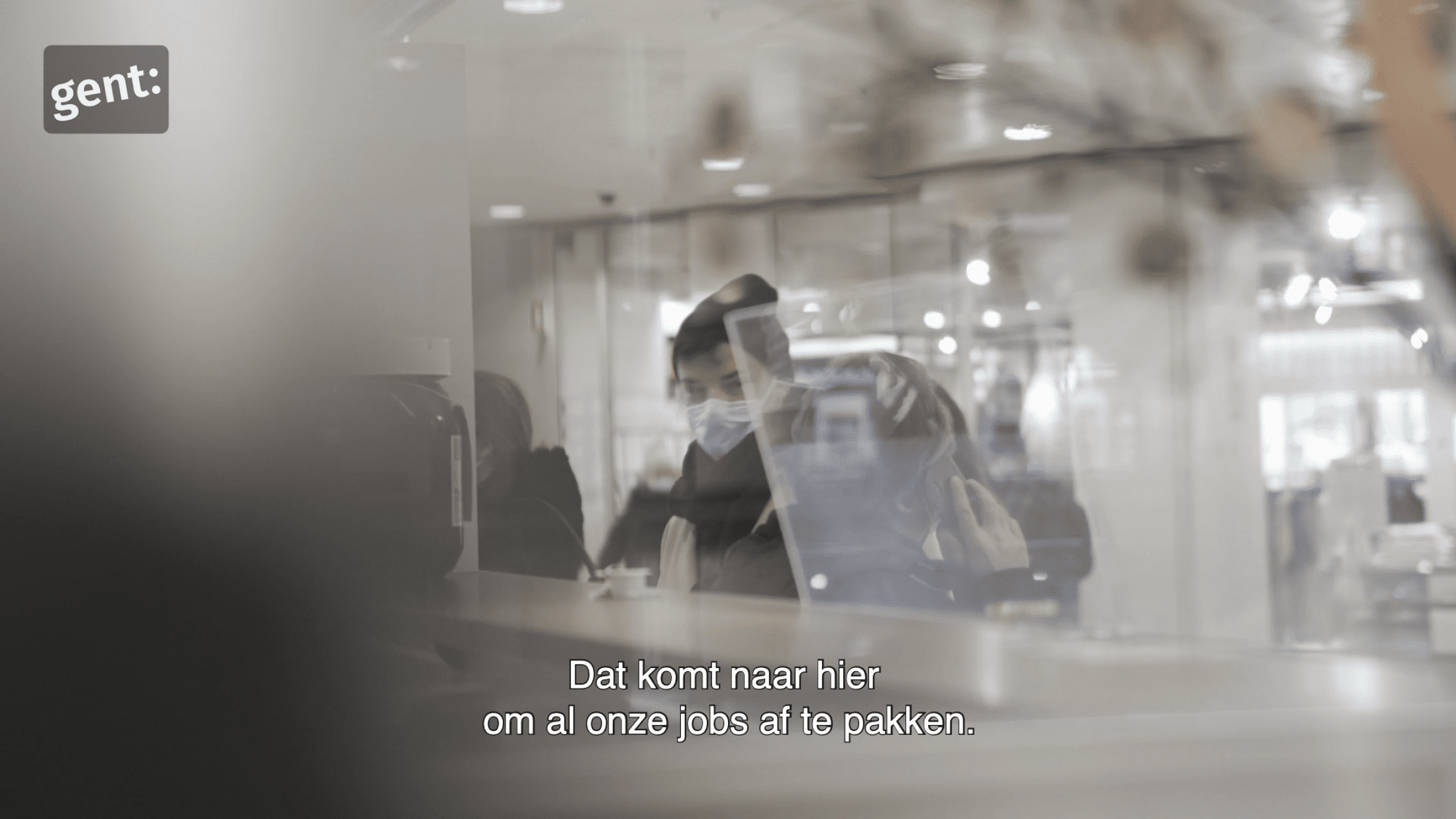 Man met mondmasker staat aan balie met ondertiteling op de voorgrond
